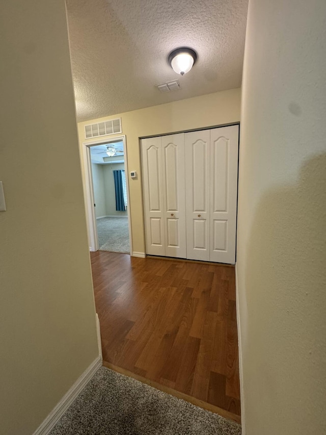 hall featuring baseboards, visible vents, and a textured ceiling