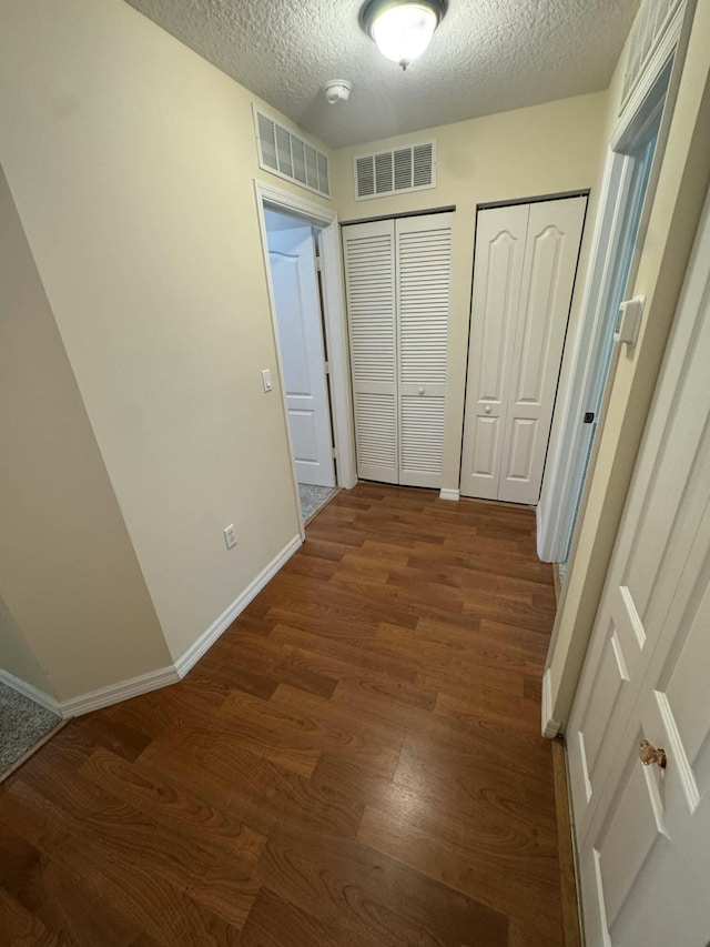 corridor featuring dark wood finished floors, visible vents, a textured ceiling, and baseboards