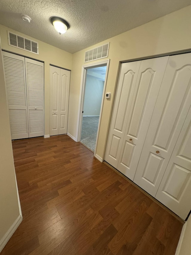 hallway featuring visible vents, a textured ceiling, baseboards, and dark wood-style flooring