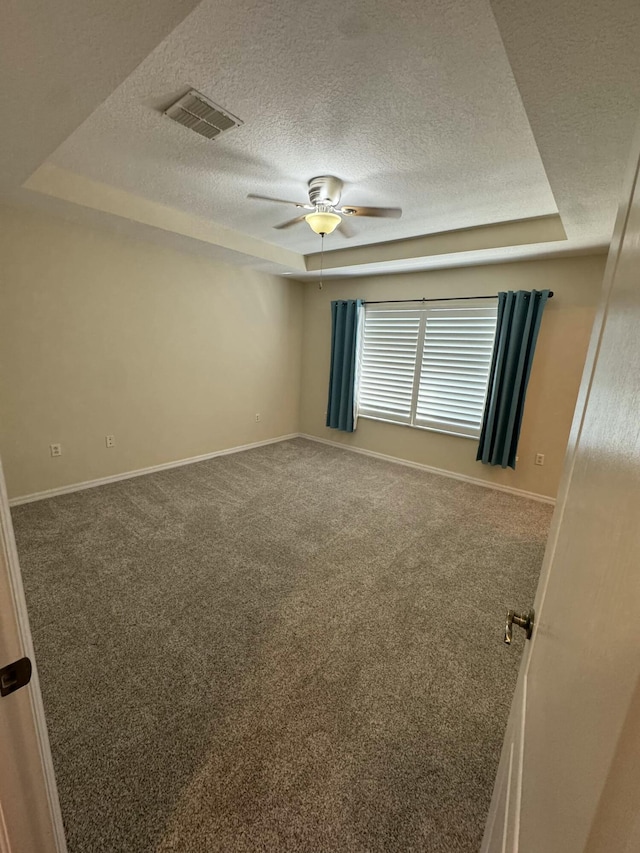 carpeted empty room with visible vents, a textured ceiling, a raised ceiling, and baseboards