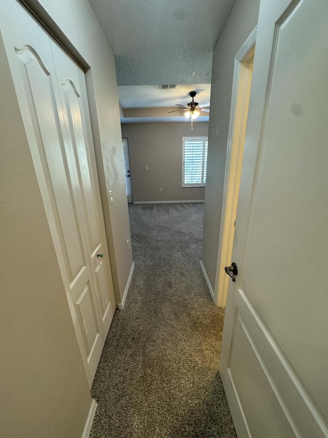 hall featuring visible vents, baseboards, a textured ceiling, and dark carpet