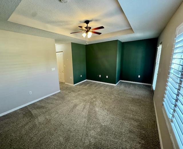 spare room featuring a raised ceiling, a ceiling fan, a textured ceiling, carpet flooring, and baseboards