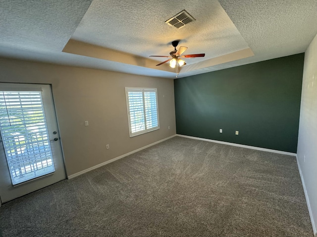 carpeted empty room with visible vents, a textured ceiling, a raised ceiling, and baseboards