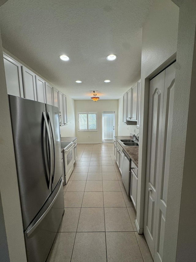 kitchen with a sink, light tile patterned floors, appliances with stainless steel finishes, and a textured ceiling