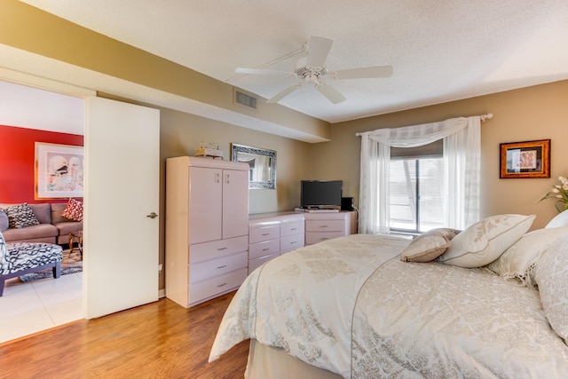 bedroom featuring a textured ceiling, wood finished floors, visible vents, and a ceiling fan