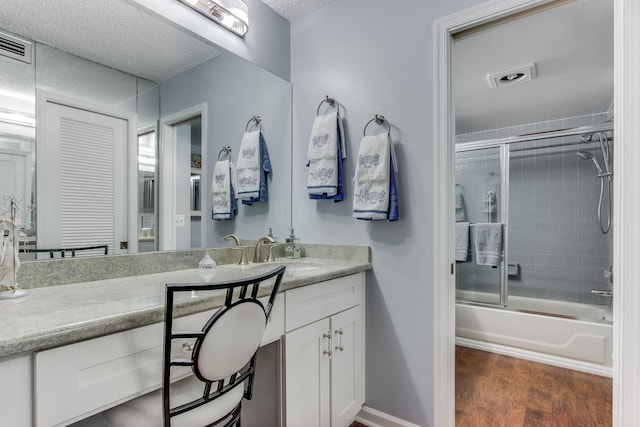 full bathroom featuring a textured ceiling, wood finished floors, visible vents, vanity, and combined bath / shower with glass door