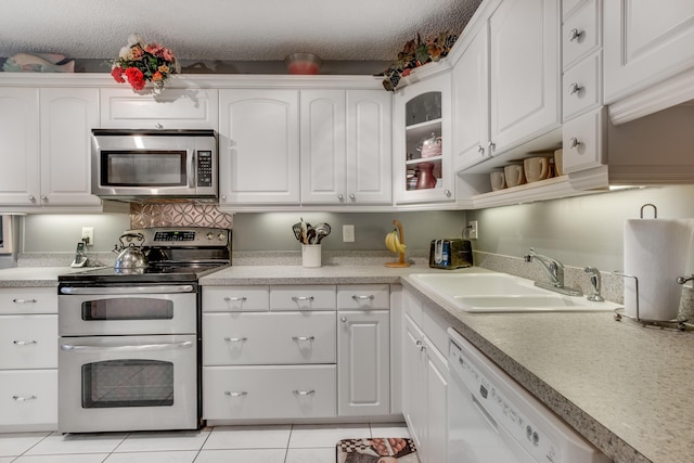 kitchen with light tile patterned floors, a sink, white cabinets, light countertops, and appliances with stainless steel finishes