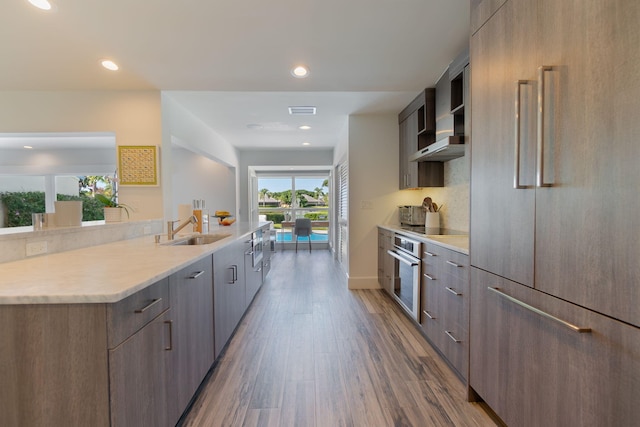 kitchen featuring oven, paneled fridge, modern cabinets, a sink, and wood finished floors