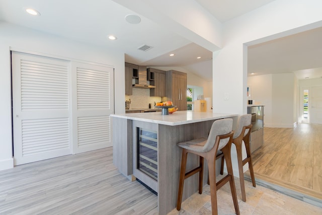 kitchen featuring a wealth of natural light, visible vents, beverage cooler, wall chimney exhaust hood, and light countertops