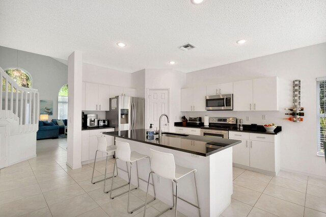 kitchen with visible vents, a sink, dark countertops, stainless steel appliances, and a breakfast bar area