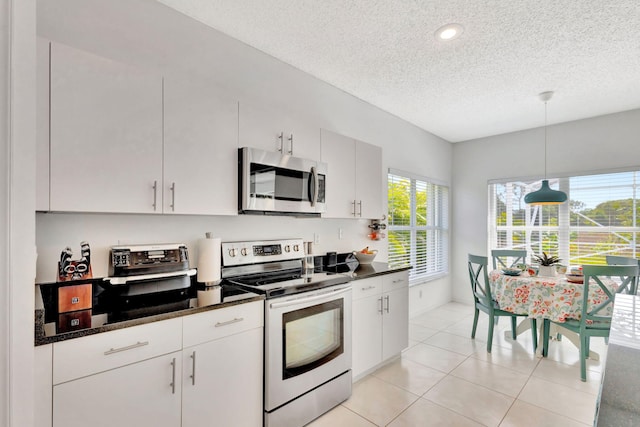 kitchen with light tile patterned floors, white cabinets, appliances with stainless steel finishes, a textured ceiling, and decorative light fixtures