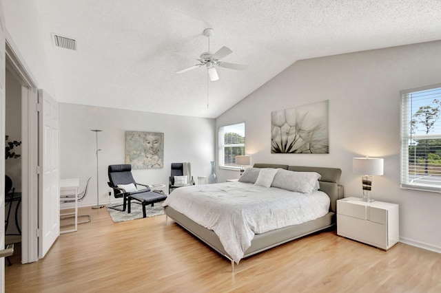 bedroom with vaulted ceiling, visible vents, light wood finished floors, and a textured ceiling