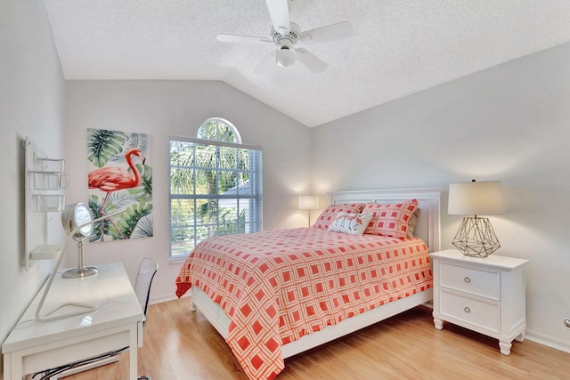 bedroom featuring baseboards, vaulted ceiling, light wood-style floors, a textured ceiling, and a ceiling fan