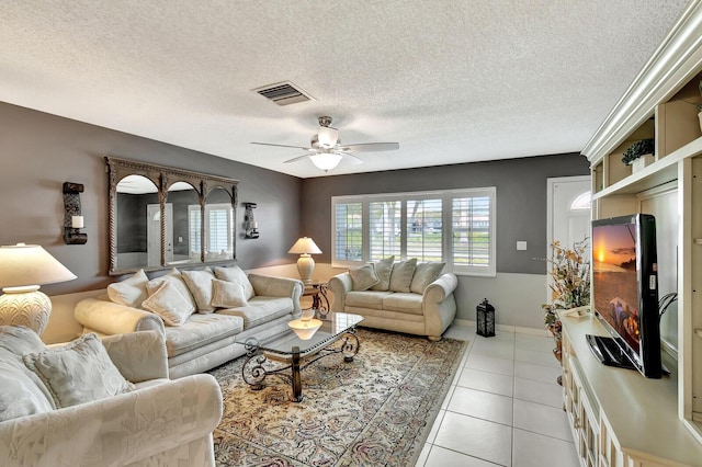 living room featuring light tile patterned floors, a textured ceiling, visible vents, and a ceiling fan