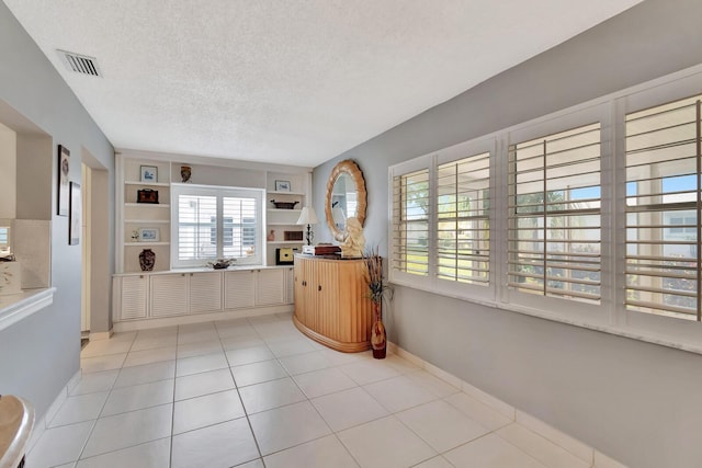 interior space featuring light tile patterned floors, baseboards, visible vents, a textured ceiling, and open shelves