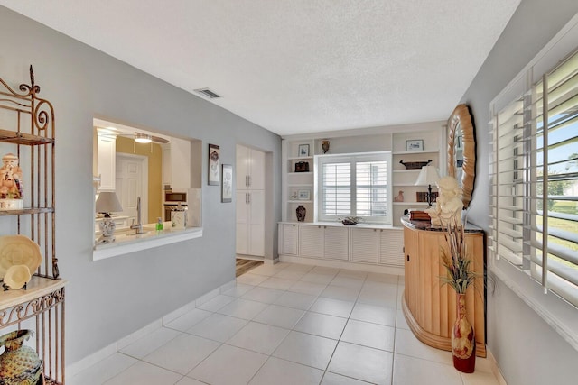 entryway featuring light tile patterned floors, baseboards, visible vents, and a textured ceiling