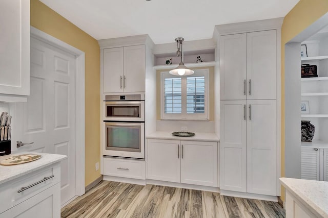 kitchen featuring pendant lighting, double oven, light wood-style floors, white cabinetry, and light stone countertops