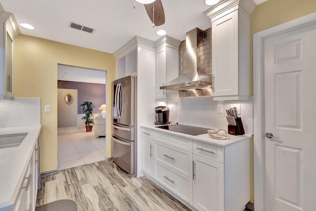 kitchen with wall chimney range hood, stainless steel fridge, black electric cooktop, and light countertops