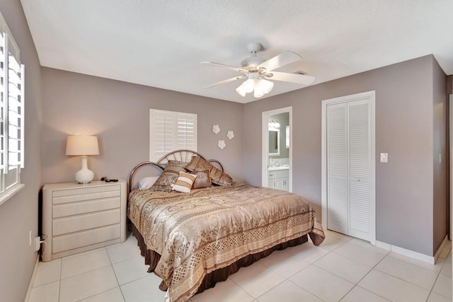 bedroom with light tile patterned floors, connected bathroom, a ceiling fan, baseboards, and a closet