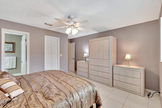 bedroom with light tile patterned floors, a closet, visible vents, a ceiling fan, and a textured ceiling