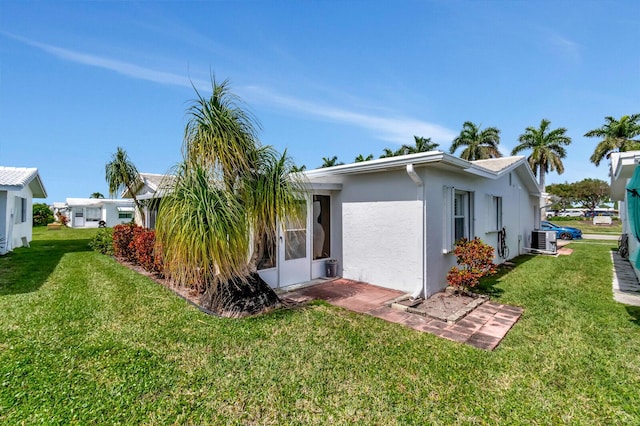 view of side of property with a lawn, central AC, and stucco siding