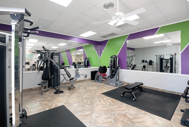 gym featuring a paneled ceiling, ceiling fan, and baseboards