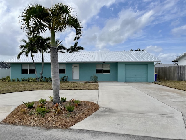 ranch-style house with fence, concrete driveway, stucco siding, metal roof, and an attached garage