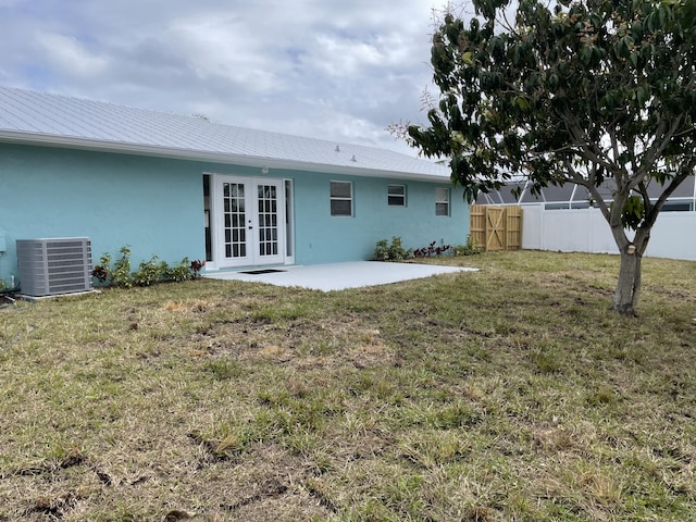 back of property featuring fence, stucco siding, cooling unit, french doors, and a lawn