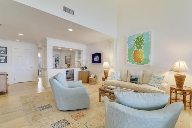 living area with wine cooler, light wood-style flooring, visible vents, ornamental molding, and decorative columns