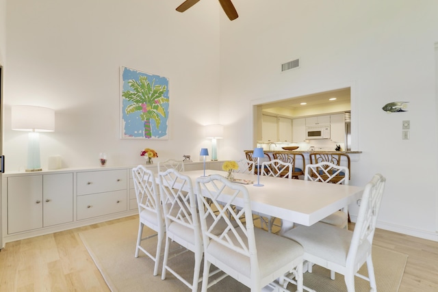 dining area featuring light wood-type flooring, ceiling fan, a towering ceiling, and visible vents