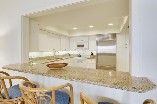 kitchen with white appliances, a tray ceiling, a sink, and recessed lighting