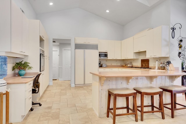 kitchen featuring high vaulted ceiling, a breakfast bar area, stone tile floors, stainless steel appliances, and a peninsula