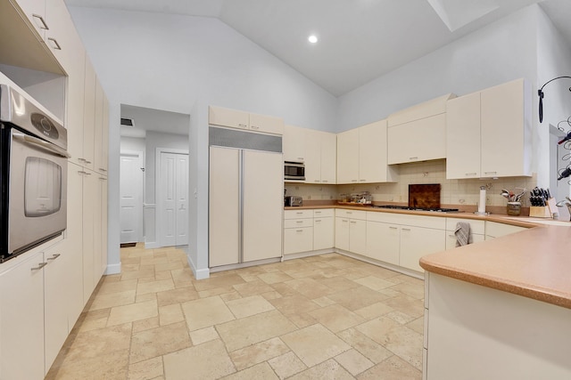 kitchen featuring stone tile floors, backsplash, built in appliances, high vaulted ceiling, and baseboards