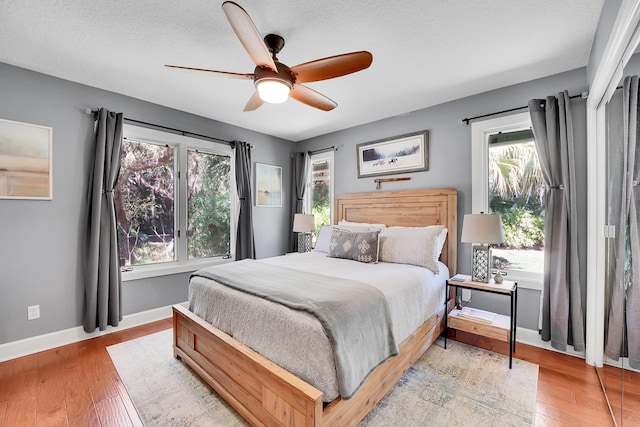 bedroom featuring light wood-type flooring, ceiling fan, a textured ceiling, and baseboards