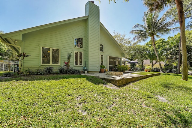 back of house featuring a patio, a lawn, and a chimney