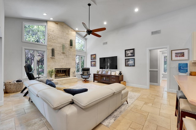 living area featuring high vaulted ceiling, a fireplace, visible vents, baseboards, and stone tile flooring