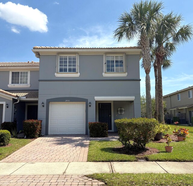 traditional-style home with stucco siding, an attached garage, a tile roof, and decorative driveway