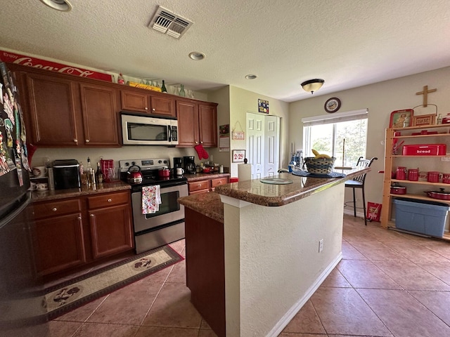 kitchen featuring visible vents, a center island, appliances with stainless steel finishes, light tile patterned flooring, and a sink