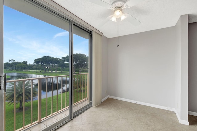 unfurnished room with light tile patterned floors, baseboards, a ceiling fan, a water view, and a textured ceiling