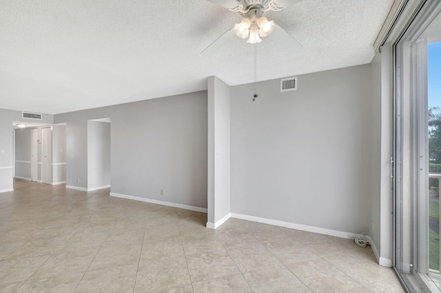 spare room featuring baseboards, ceiling fan, visible vents, and a textured ceiling