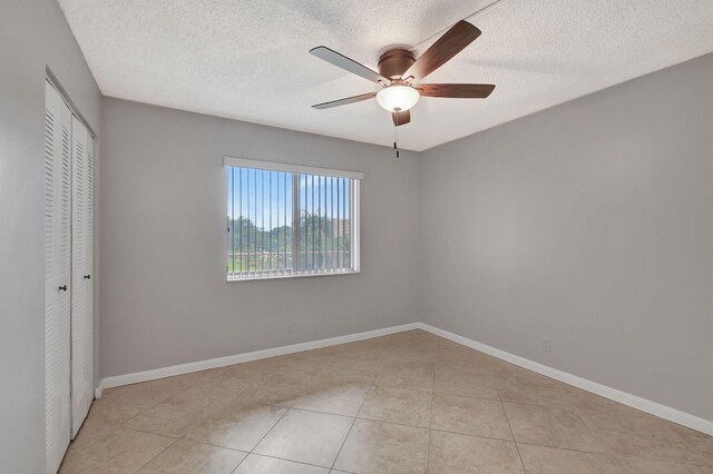 unfurnished bedroom with light tile patterned floors, a closet, a textured ceiling, and baseboards