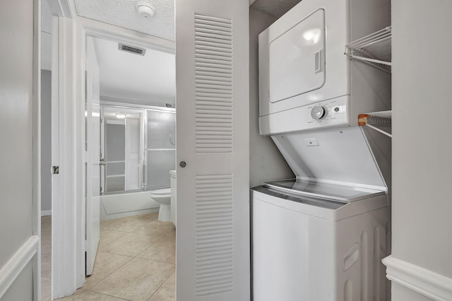 clothes washing area with a textured ceiling, light tile patterned flooring, stacked washer and dryer, laundry area, and visible vents