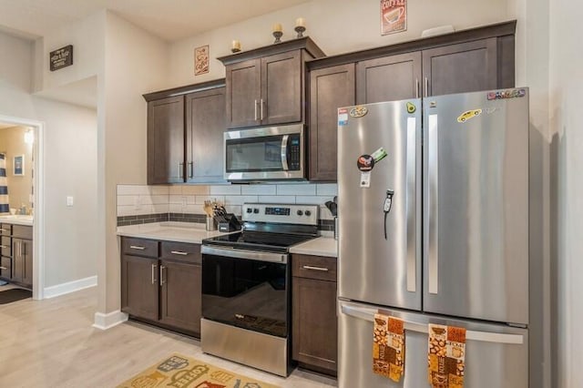 kitchen featuring light wood-type flooring, backsplash, stainless steel appliances, dark brown cabinetry, and light countertops