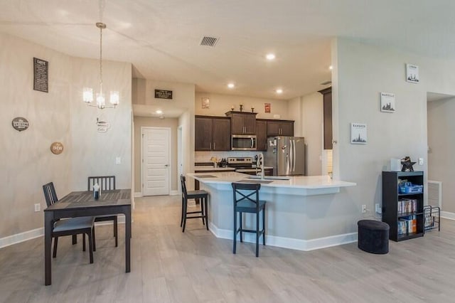 kitchen with visible vents, dark brown cabinetry, light countertops, appliances with stainless steel finishes, and a kitchen bar