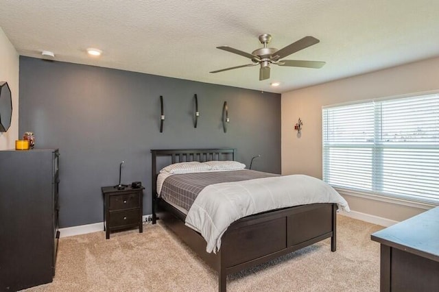 bedroom featuring baseboards, light colored carpet, a ceiling fan, and a textured ceiling