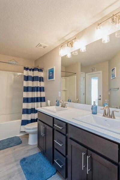 full bath featuring visible vents, toilet, double vanity, a textured ceiling, and a sink