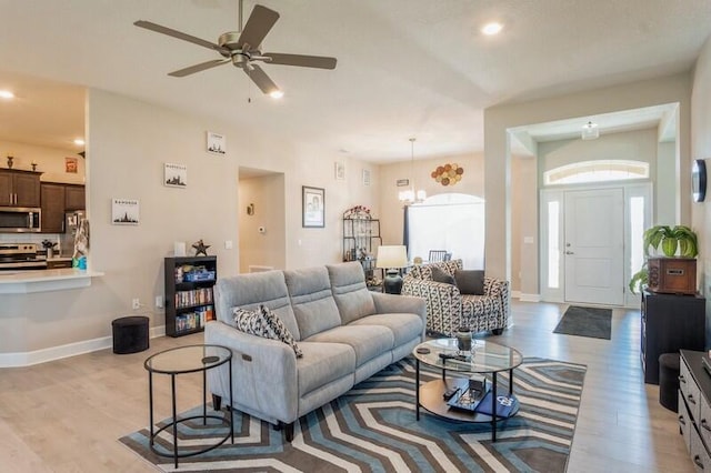 living room with light wood finished floors, recessed lighting, ceiling fan with notable chandelier, and baseboards