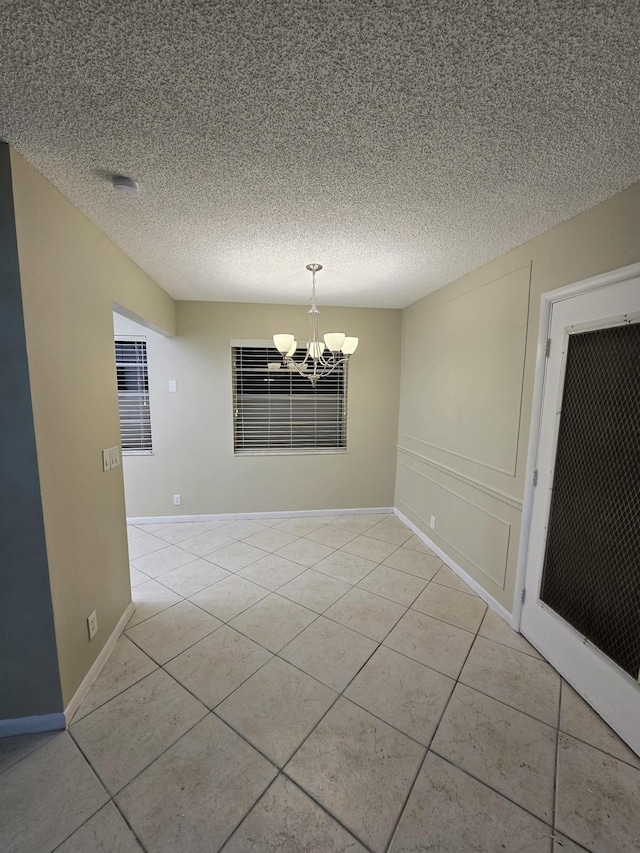 unfurnished room with a textured ceiling, light tile patterned flooring, baseboards, and a chandelier