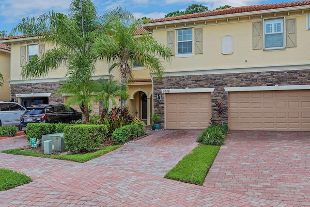 view of front of house with driveway, stone siding, a tile roof, and stucco siding