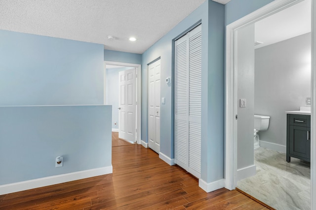 corridor with a textured ceiling, baseboards, and wood finished floors